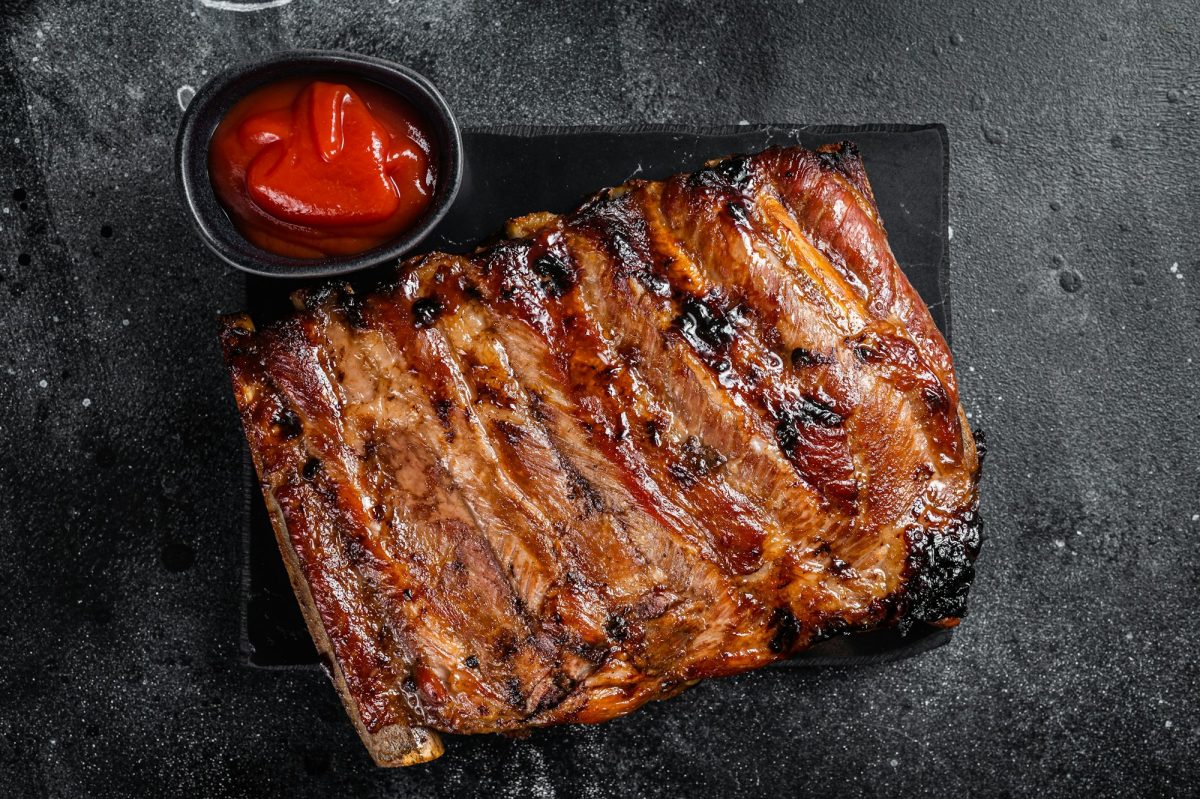 Full rack of BBQ grilled pork spare ribs on a marble board. Black background. Top view