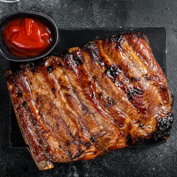 Full rack of BBQ grilled pork spare ribs on a marble board. Black background. Top view