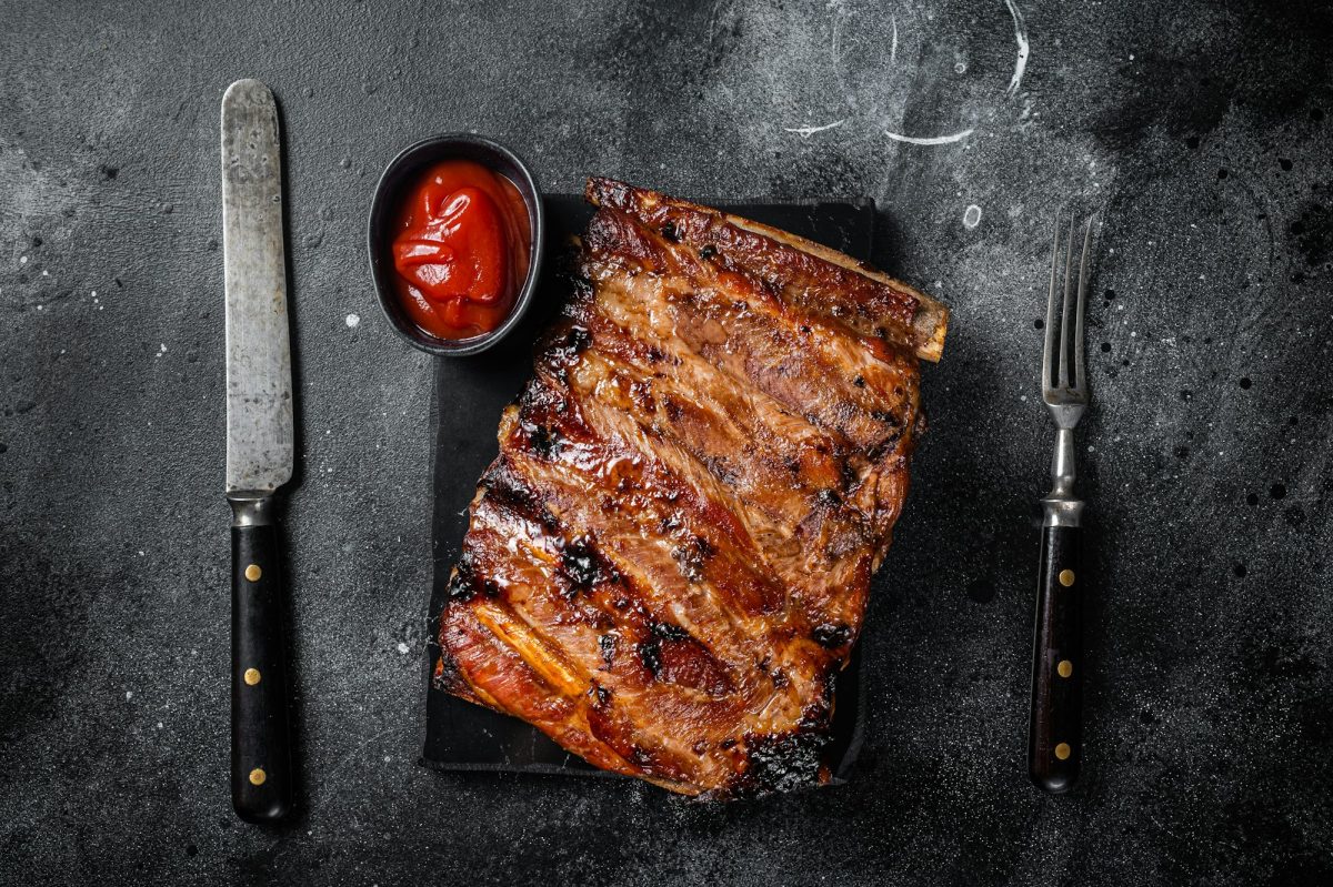 Full rack of BBQ grilled pork spare ribs on a marble board. Black background. Top view