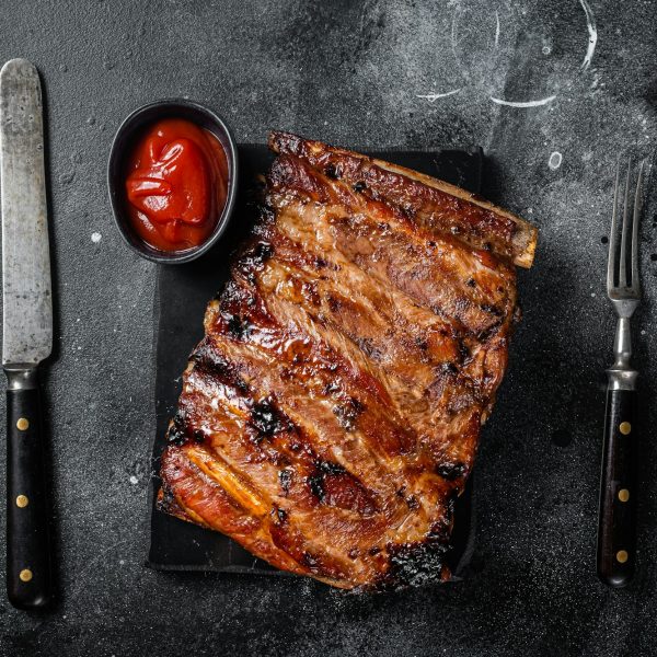 Full rack of BBQ grilled pork spare ribs on a marble board. Black background. Top view