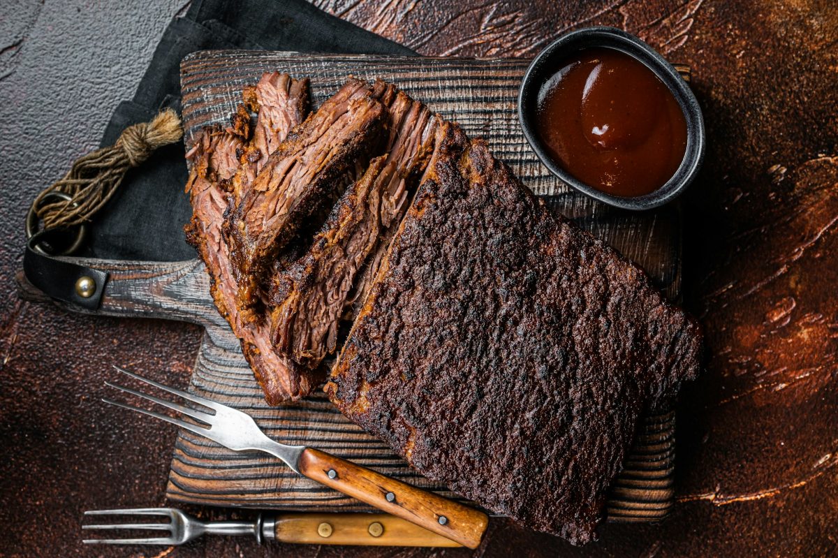 Traditional smoked barbecue wagyu beef brisket on wooden board. Dark background. Top view