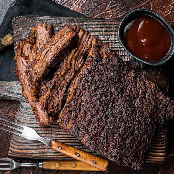 Traditional smoked barbecue wagyu beef brisket on wooden board. Dark background. Top view